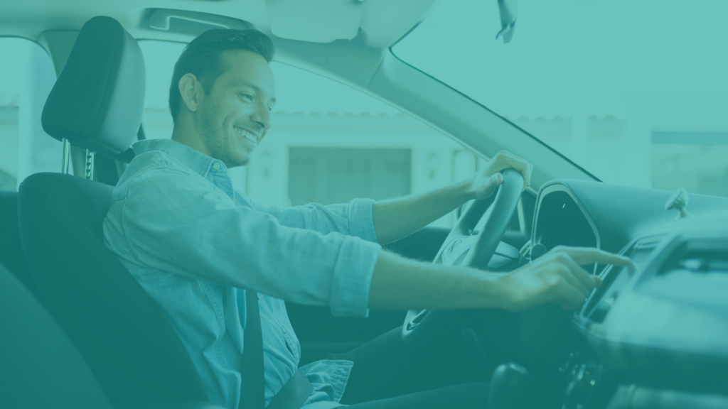 Man driving a car smiles as he taps on the screen of the radio player.